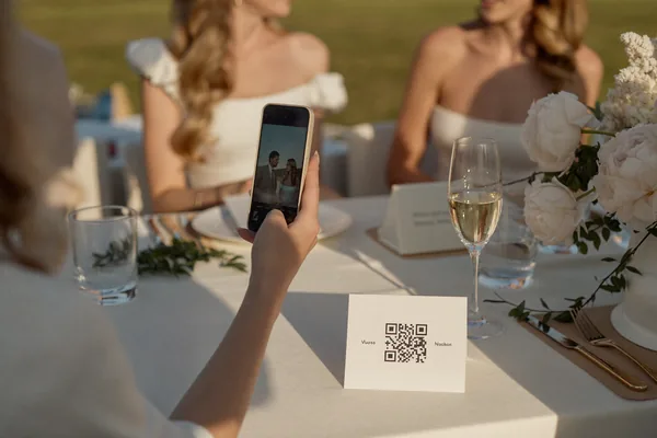 A guest scanning the small printed QR card on a wedding reception table with her phone